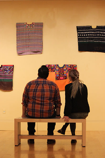 Two students in the gallery viewing huipiles as part of the Hispanidad! exhibit.